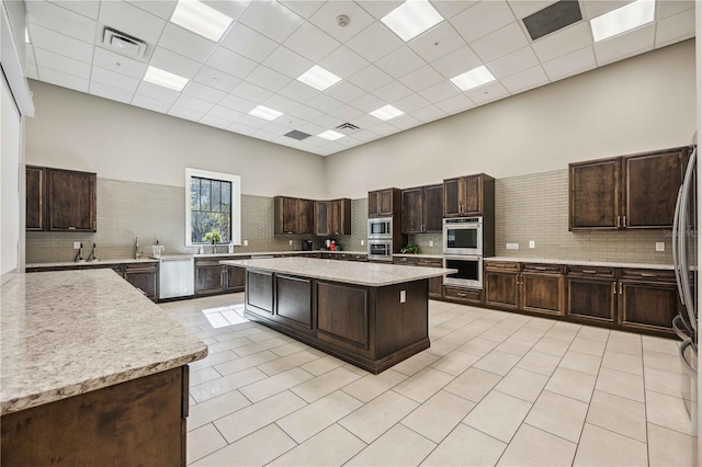 kitchen featuring a center island, a drop ceiling, stainless steel appliances, a towering ceiling, and dark brown cabinets