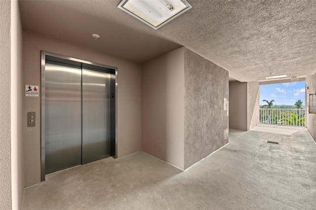 hallway with light carpet, elevator, and a textured ceiling