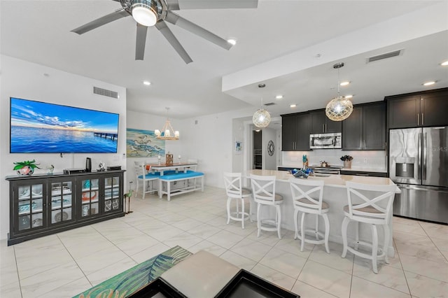 kitchen featuring tasteful backsplash, hanging light fixtures, appliances with stainless steel finishes, a kitchen breakfast bar, and a kitchen island with sink