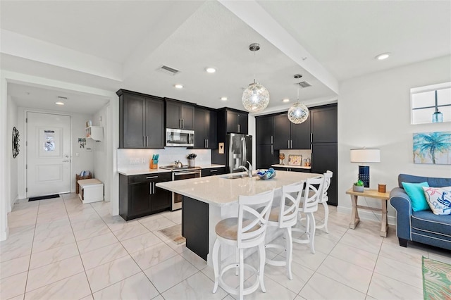 kitchen with sink, hanging light fixtures, a center island with sink, appliances with stainless steel finishes, and a kitchen breakfast bar