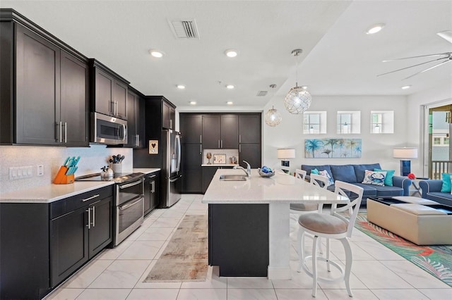 kitchen featuring sink, a breakfast bar, appliances with stainless steel finishes, hanging light fixtures, and an island with sink