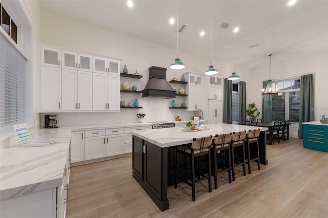 kitchen with hanging light fixtures, a kitchen breakfast bar, an island with sink, white cabinets, and custom exhaust hood