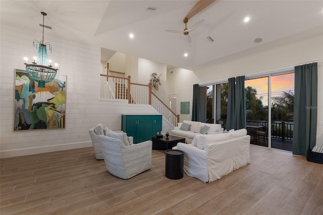 living room with ceiling fan with notable chandelier, hardwood / wood-style flooring, and high vaulted ceiling