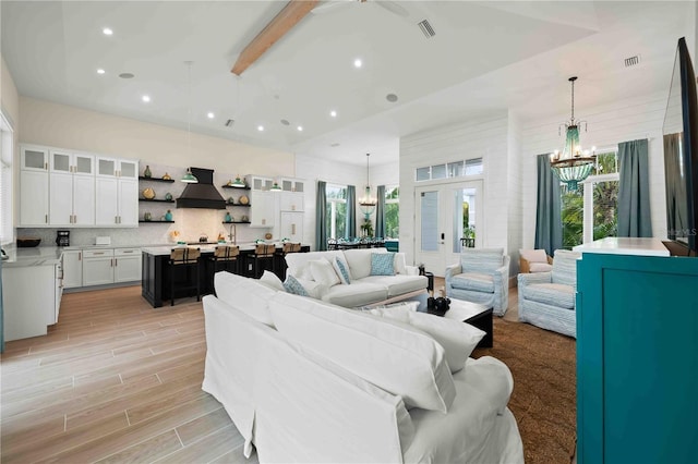 living room featuring beamed ceiling, french doors, and an inviting chandelier