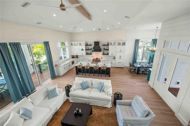 living room featuring beamed ceiling, ceiling fan with notable chandelier, and light hardwood / wood-style flooring