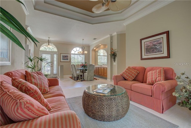 tiled living room with ceiling fan with notable chandelier, a raised ceiling, and ornamental molding