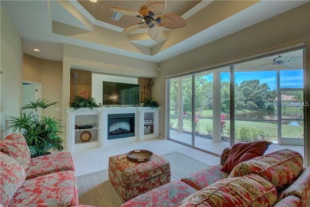 carpeted living room featuring a raised ceiling, ceiling fan, and ornamental molding