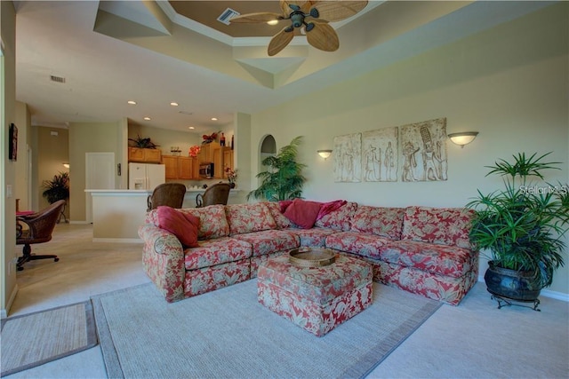 living room featuring ceiling fan, light colored carpet, ornamental molding, and a tray ceiling