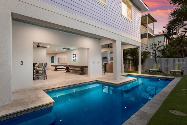 pool at dusk featuring ceiling fan and a patio