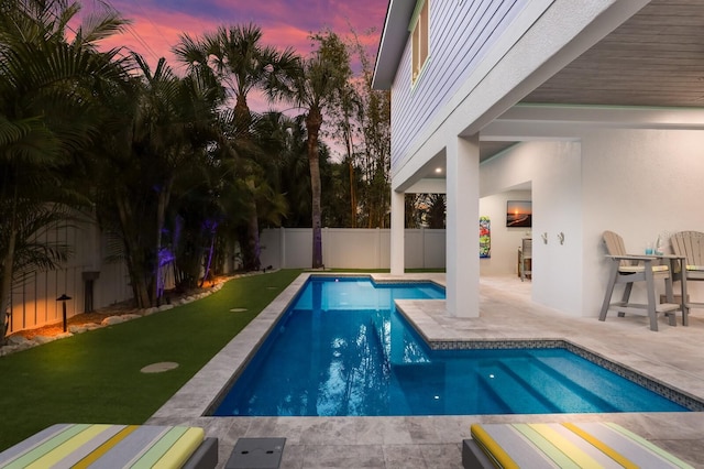 pool at dusk featuring a yard and a patio