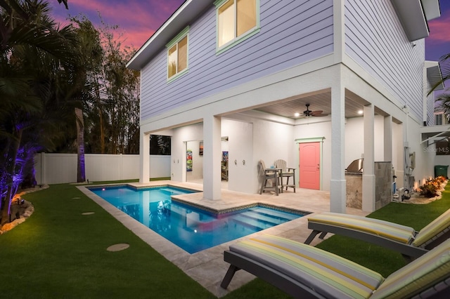 pool at dusk featuring area for grilling, a patio area, ceiling fan, and an outdoor bar