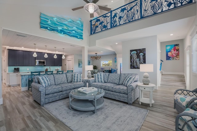 living room with ceiling fan with notable chandelier, light hardwood / wood-style floors, and a towering ceiling