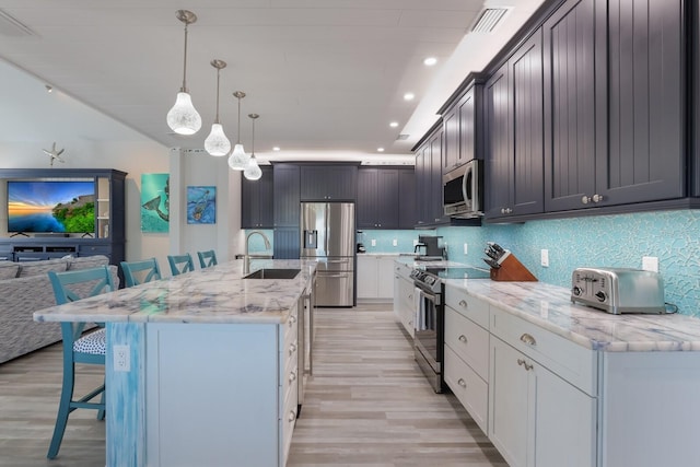 kitchen featuring a kitchen bar, appliances with stainless steel finishes, sink, hanging light fixtures, and an island with sink