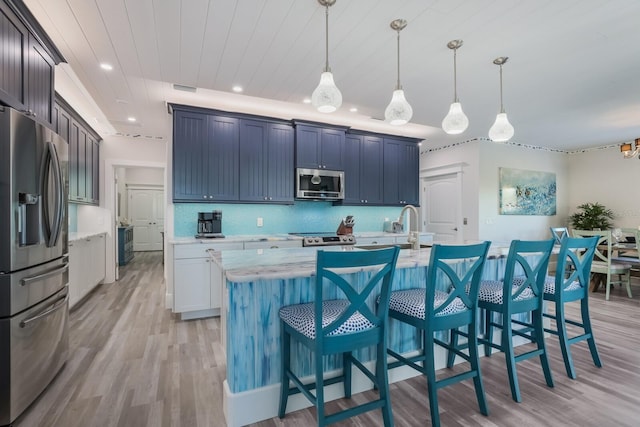 kitchen featuring decorative backsplash, light wood-type flooring, stainless steel appliances, pendant lighting, and a center island with sink