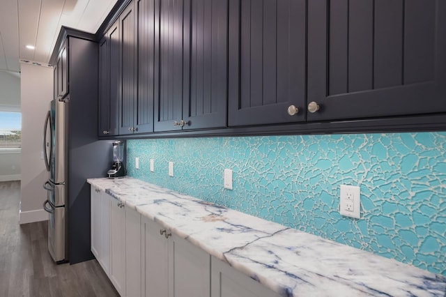 kitchen with stainless steel fridge, tasteful backsplash, light stone counters, hardwood / wood-style floors, and white cabinetry