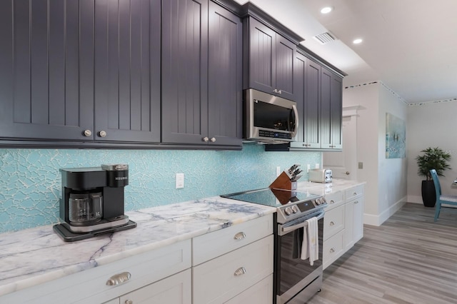 kitchen featuring white cabinetry, stainless steel appliances, light stone counters, light hardwood / wood-style flooring, and decorative backsplash