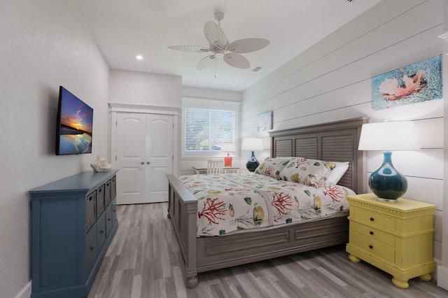 bedroom with wood-type flooring, a closet, ceiling fan, and wooden walls