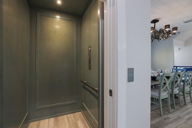 corridor with a notable chandelier, elevator, and light hardwood / wood-style flooring