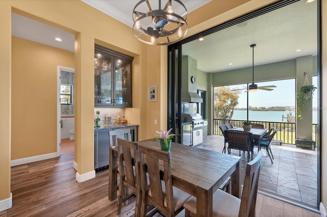 dining area with ceiling fan with notable chandelier, a water view, hardwood / wood-style flooring, and crown molding