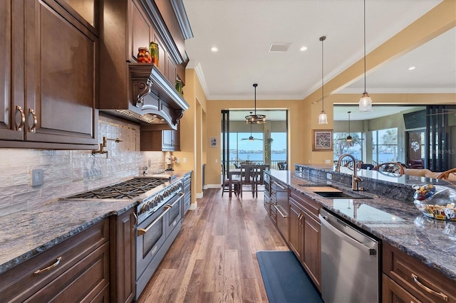 kitchen with dark brown cabinetry, hanging light fixtures, stainless steel appliances, dark hardwood / wood-style flooring, and dark stone countertops