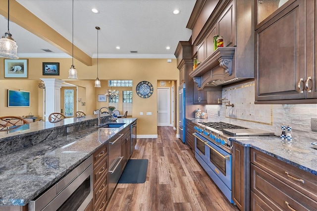 kitchen with built in appliances, decorative light fixtures, dark stone countertops, and sink