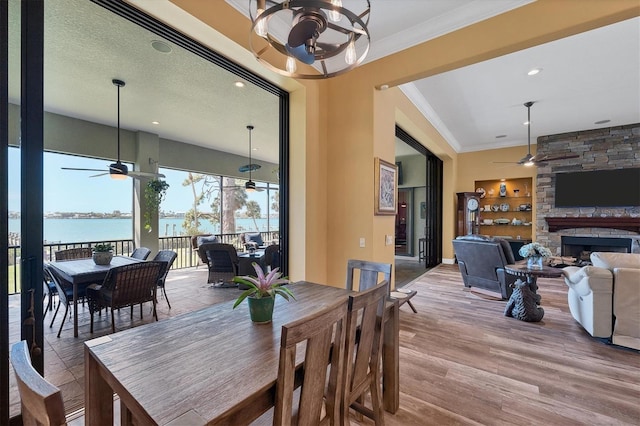 dining area featuring a water view, crown molding, light wood-type flooring, a textured ceiling, and a fireplace