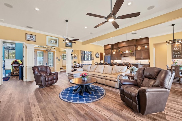 living room featuring hardwood / wood-style flooring, ceiling fan with notable chandelier, ornamental molding, and decorative columns