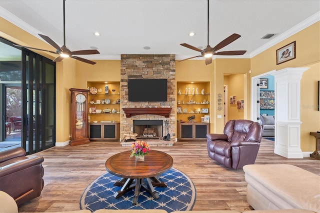 living room with built in shelves, ornate columns, wood-type flooring, a fireplace, and ornamental molding