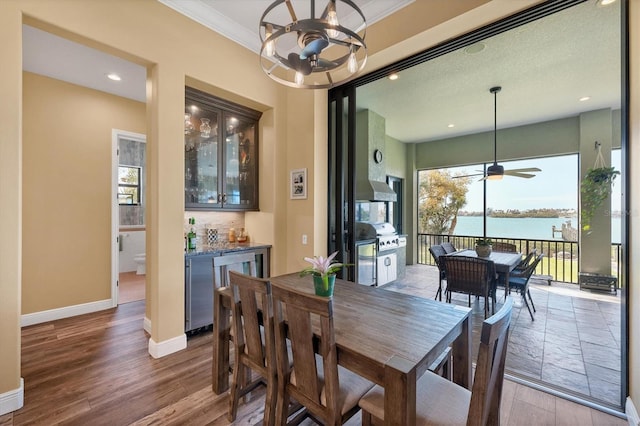 dining space featuring ceiling fan with notable chandelier, baseboards, wood finished floors, a water view, and a bar