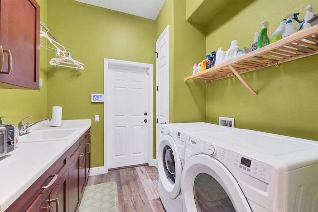 laundry area with cabinet space, a sink, baseboards, light wood-style flooring, and washer and clothes dryer