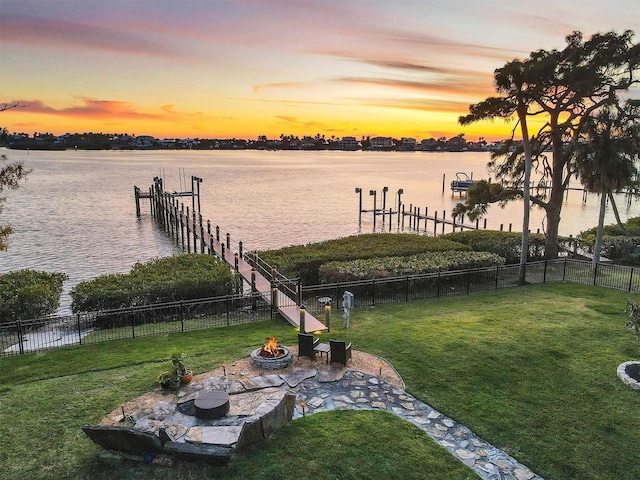 dock area with a yard, a water view, fence, and a fire pit