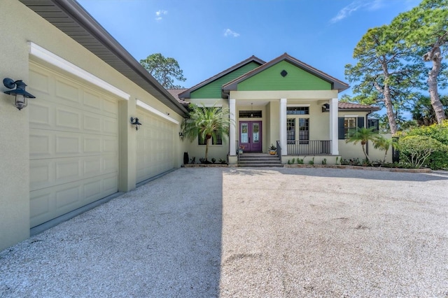 view of front facade featuring covered porch, driveway, french doors, and stucco siding