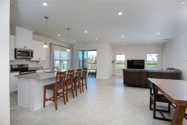 kitchen featuring stainless steel appliances, light stone counters, decorative light fixtures, a kitchen island with sink, and white cabinets