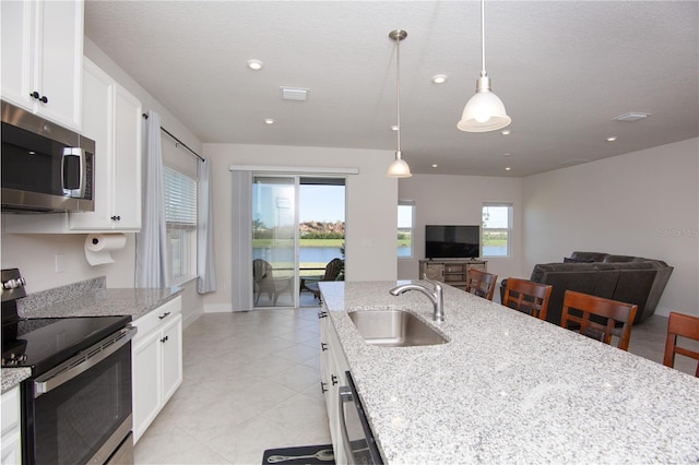 kitchen with sink, hanging light fixtures, light stone countertops, white cabinetry, and stainless steel appliances