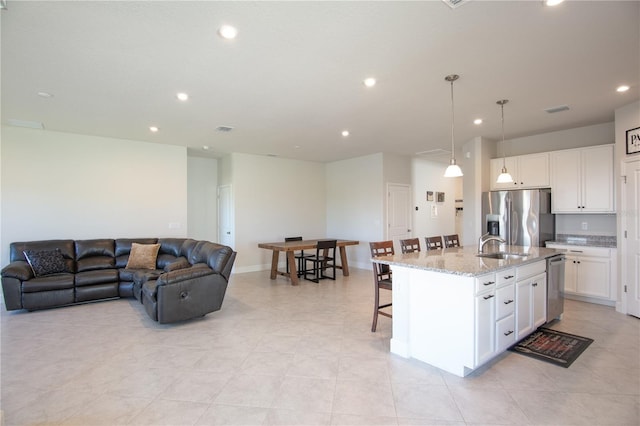 kitchen with pendant lighting, a center island with sink, light stone counters, white cabinetry, and stainless steel appliances