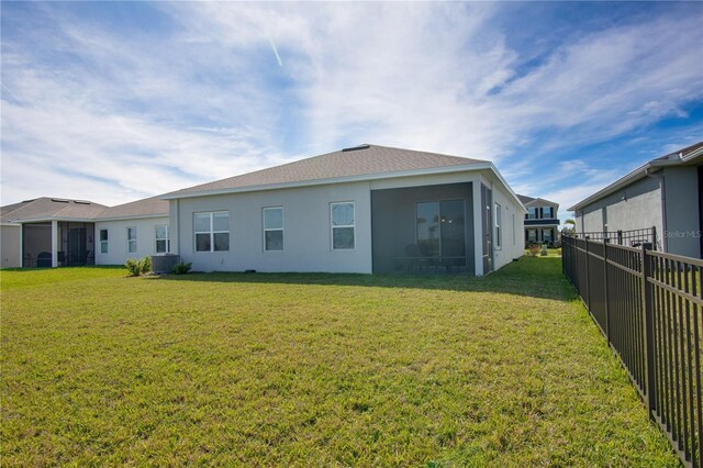 rear view of property with a yard, stucco siding, fence, and central air condition unit