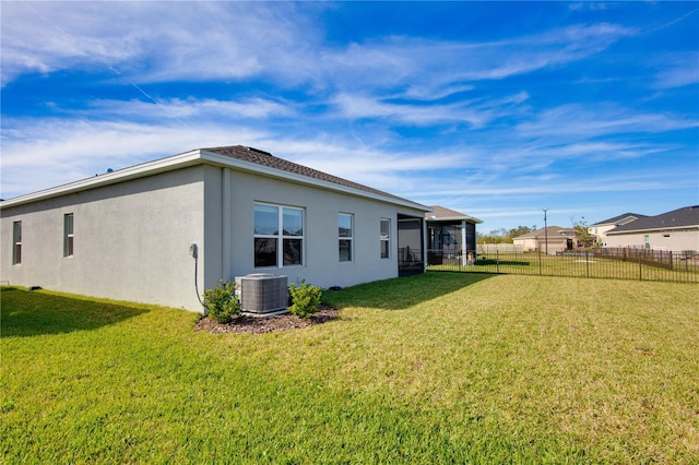 rear view of property featuring central air condition unit, a lawn, fence, and stucco siding