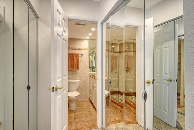 bathroom with tile patterned flooring, an enclosed shower, toilet, vanity, and tile walls