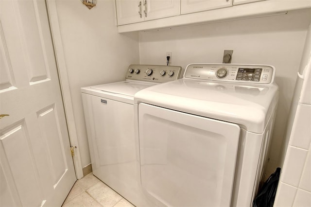 laundry room featuring washing machine and clothes dryer, light tile patterned floors, and cabinets