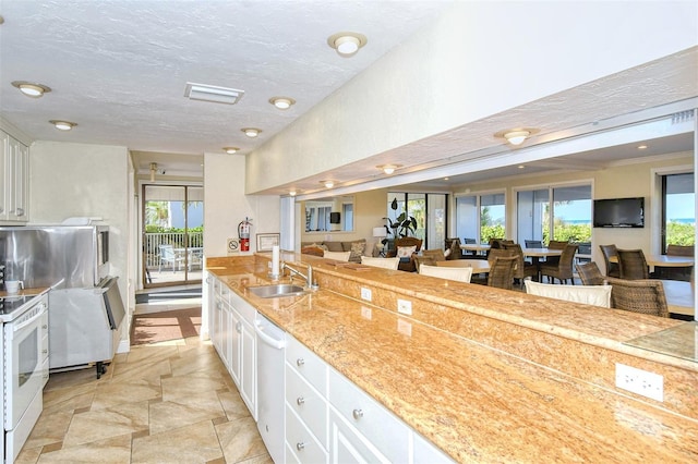 kitchen with white appliances, white cabinets, sink, light stone counters, and a breakfast bar area