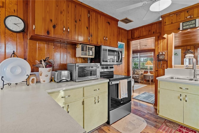 kitchen featuring ceiling fan, sink, a textured ceiling, wooden walls, and appliances with stainless steel finishes