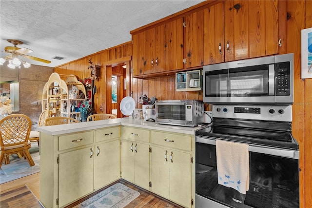 kitchen with kitchen peninsula, a textured ceiling, stainless steel appliances, ceiling fan, and wood walls