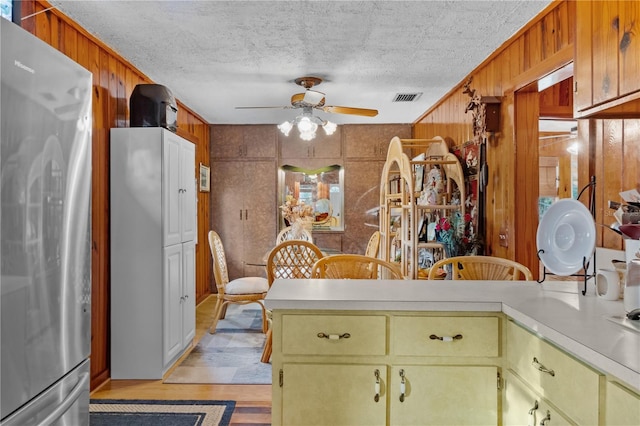 kitchen featuring ceiling fan, stainless steel fridge, a textured ceiling, and wooden walls