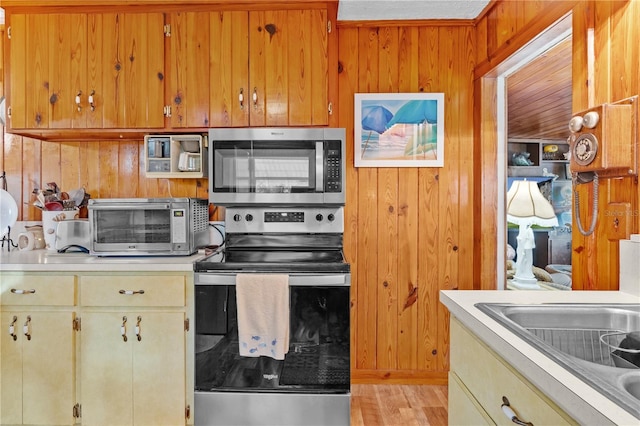 kitchen featuring wooden walls, light hardwood / wood-style flooring, and stainless steel appliances