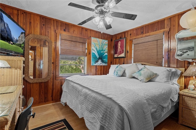 bedroom with ceiling fan, wood walls, and light wood-type flooring