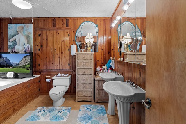 bathroom with a textured ceiling, double sink, and wood walls