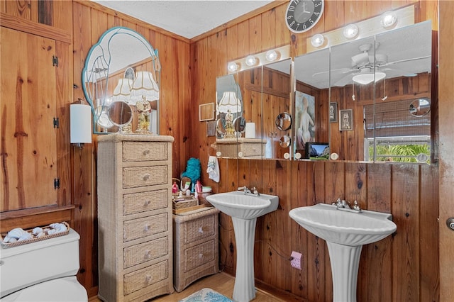 bathroom featuring wooden walls, ceiling fan, toilet, a textured ceiling, and double sink