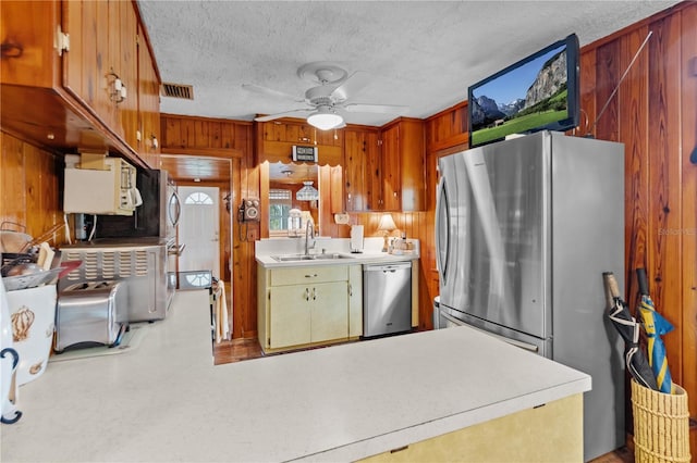 kitchen featuring sink, wooden walls, ceiling fan, a textured ceiling, and appliances with stainless steel finishes