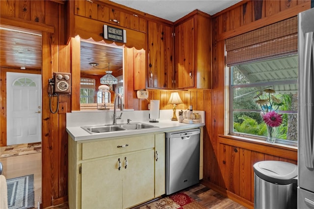 kitchen with appliances with stainless steel finishes, hardwood / wood-style flooring, wood walls, and sink