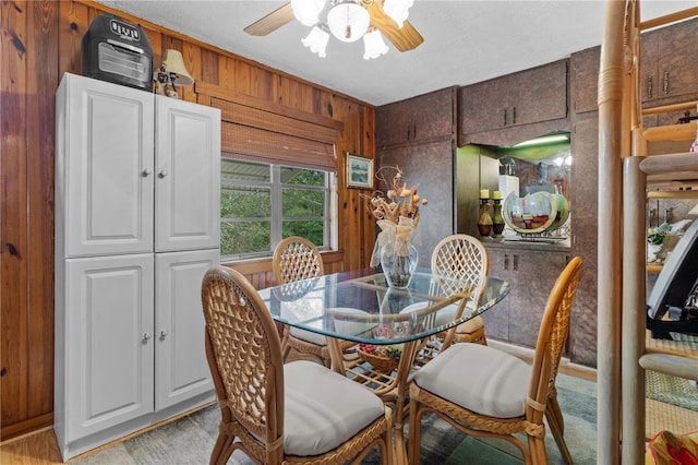 dining space featuring ceiling fan and wooden walls